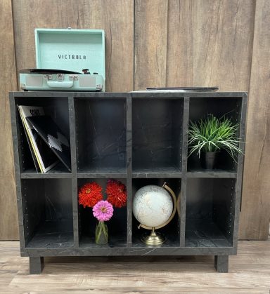 A stylish wooden shelf with a globe, vinyl records, plants, and colorful flowers.